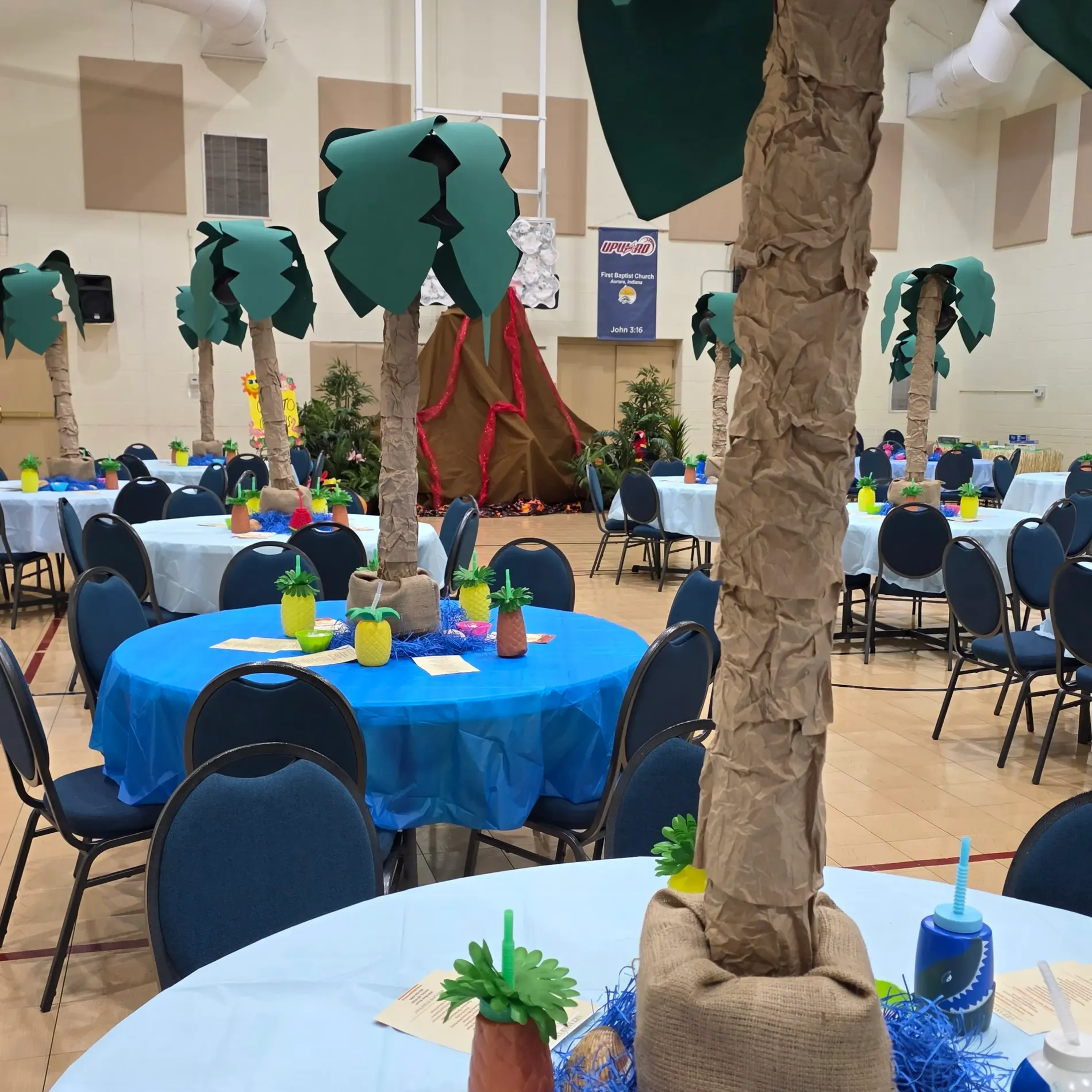 Decorated tables with palm tree centerpieces in a large hall.