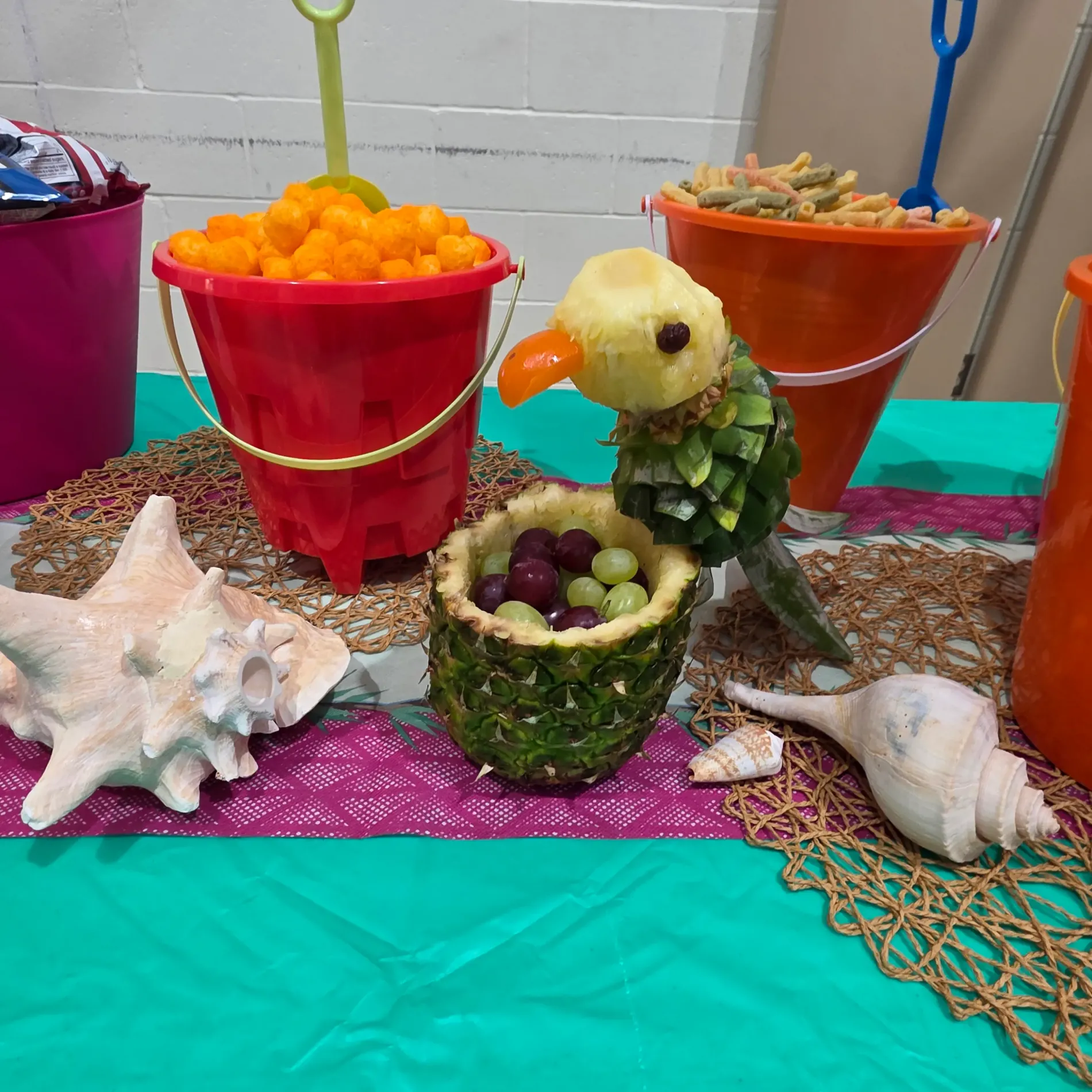Tropical-themed table with fruit parrot and colorful snack buckets.