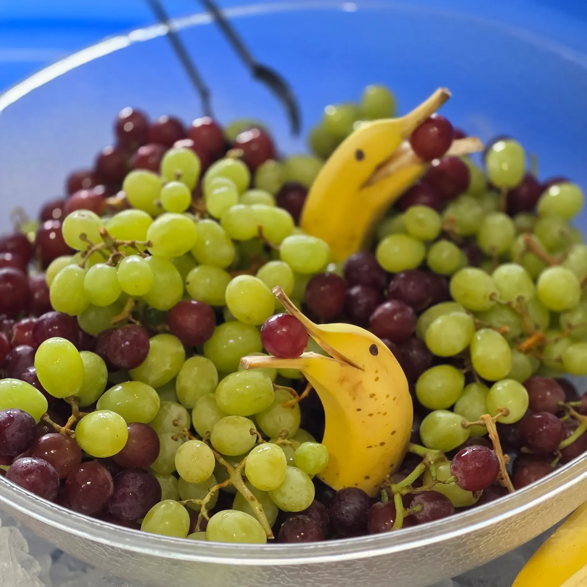 Bowl of grapes with banana dolphins holding grapes.