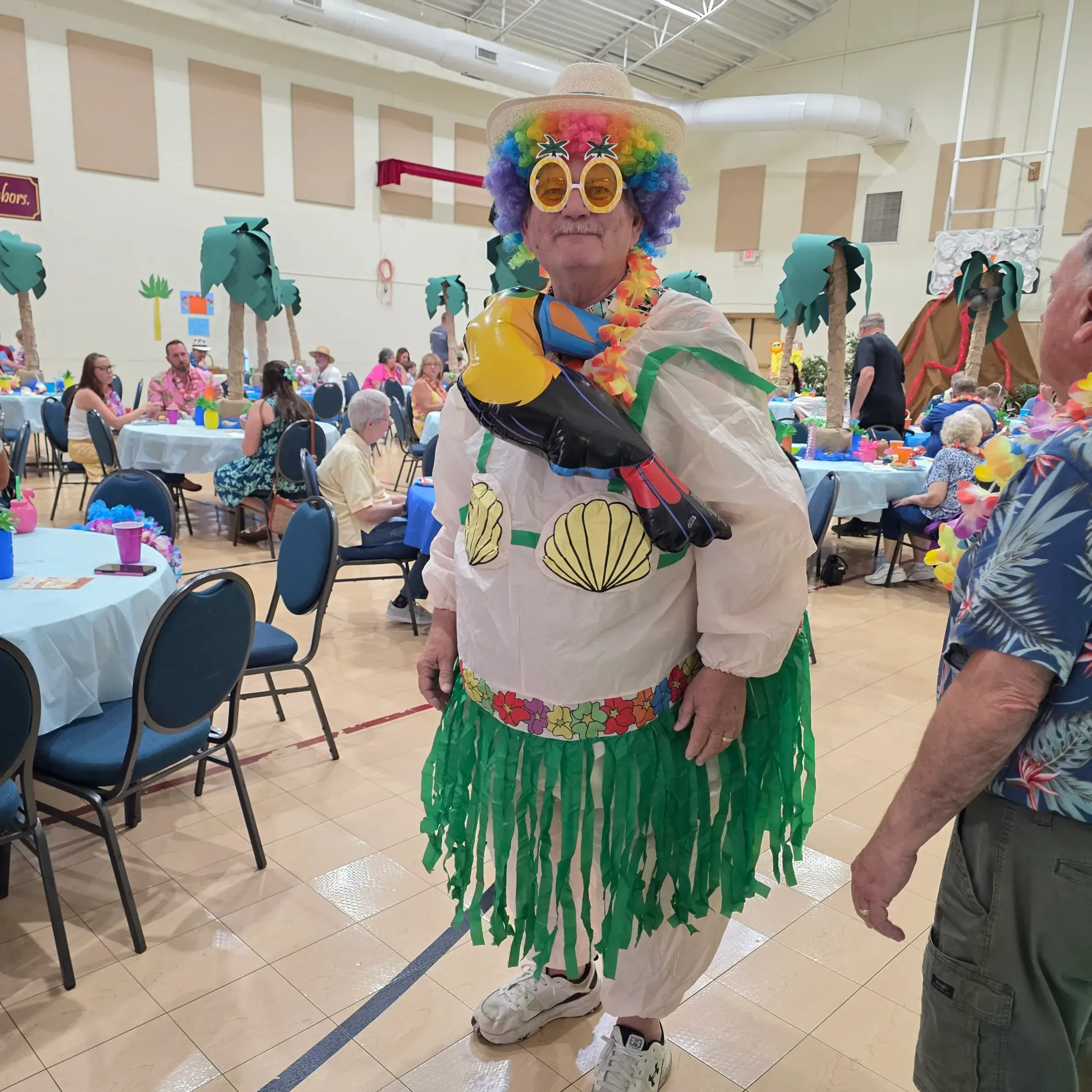 Man in a colorful costume with a grass skirt and parrot, at a festive gathering.