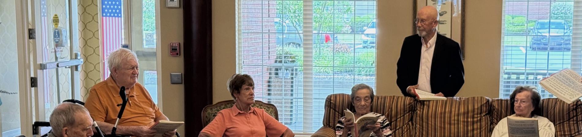 Elderly group in a cozy room, seated on sofas, reading together.