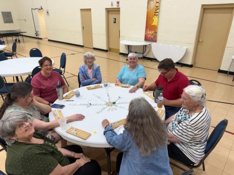 A group of senior people playing a board game around a round table indoors.
