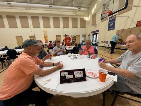 Seniors playing cards at a round table in a community hall.