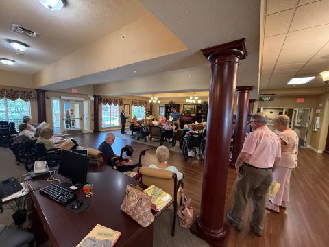 A group of elderly people gather in a spacious room with large columns.