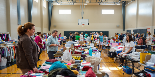 Indoor market in a gym, people browsing tables with clothes and items.