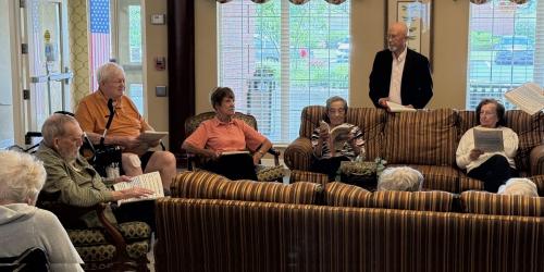 Elderly group in a cozy room, seated on sofas, reading together.